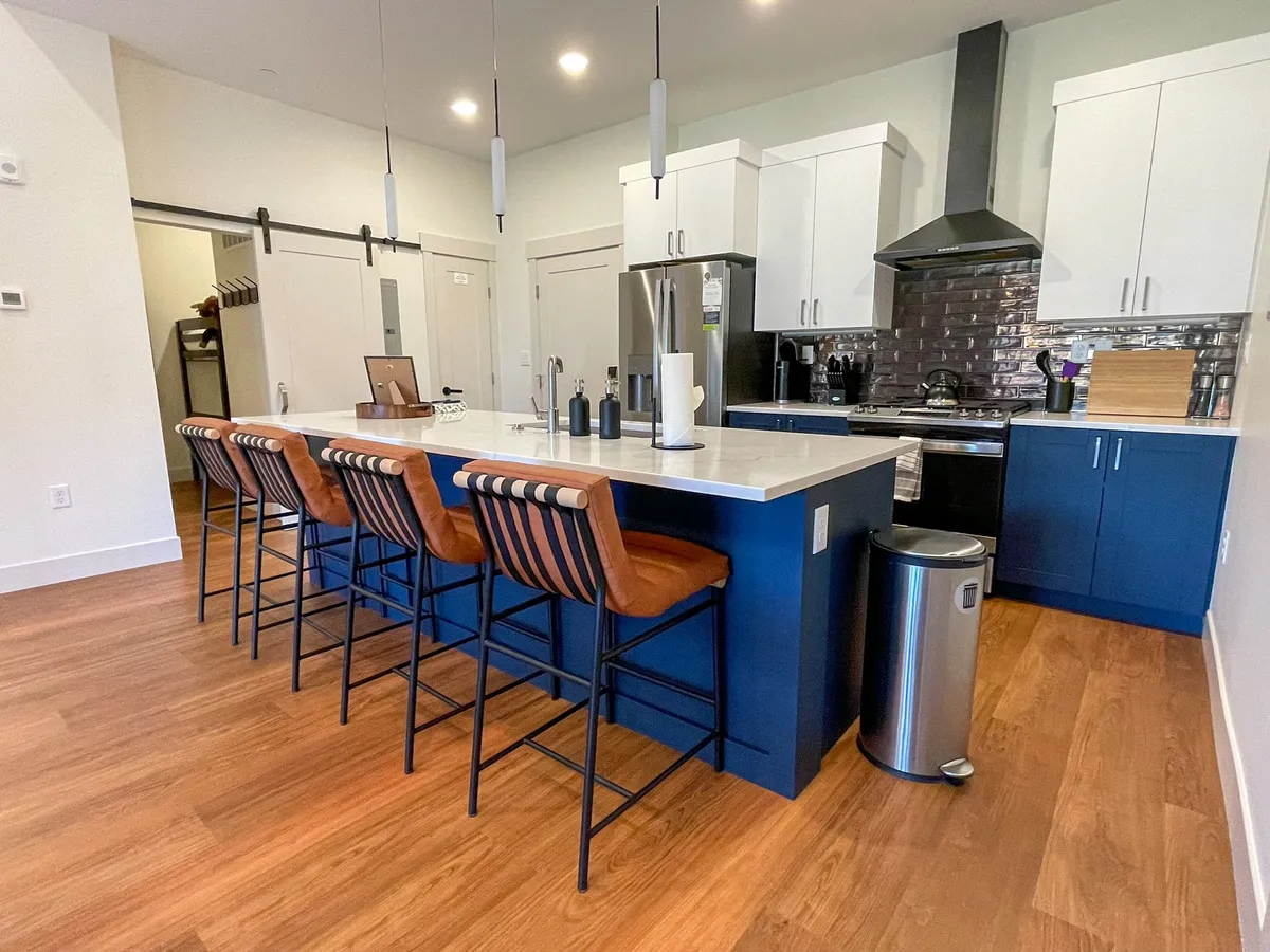 A stylish kitchen with a central island featuring bar stools, stainless steel appliances, and modern cabinetry. The space is designed for cooking and casual dining, with an inviting atmosphere for gatherings or morning coffee.