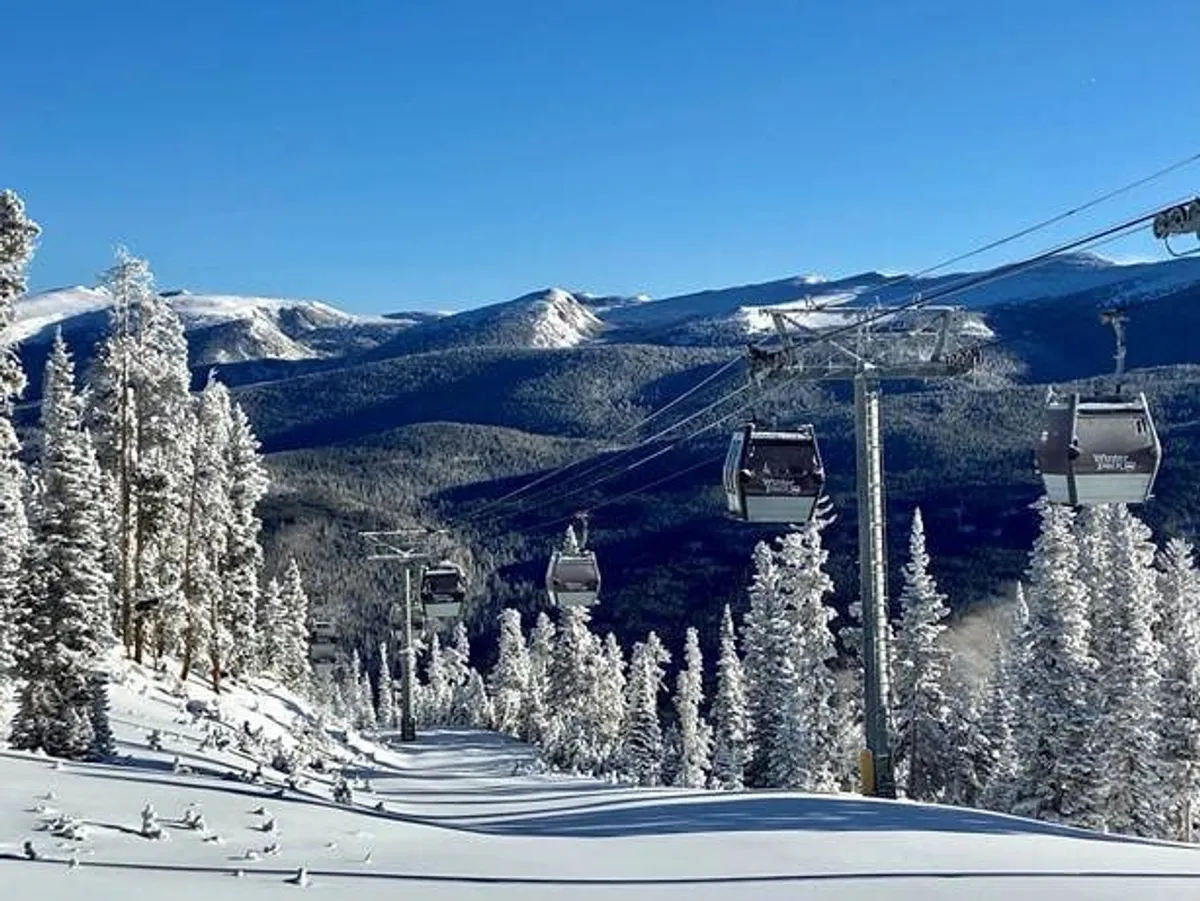 A scenic winter landscape featuring a ski lift gliding above snow-covered trees and an expansive mountain range in the background. The sky is crisp and clear, emphasizing the exhilarating outdoor adventure possibilities available nearby.