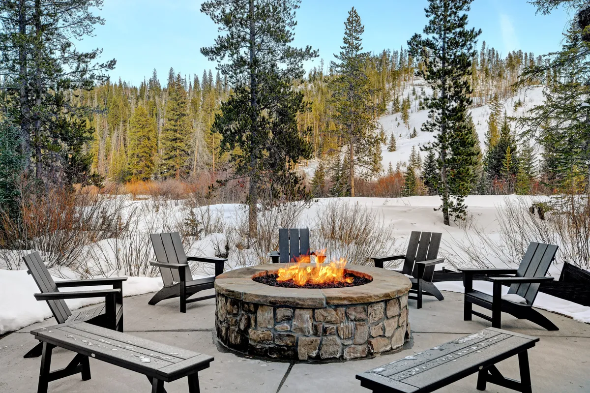 A cozy outdoor fire pit area set against a backdrop of trees and snow, with comfortable seating perfect for gathering, warming up after a day outside, or enjoying starlit evenings with friends and family.