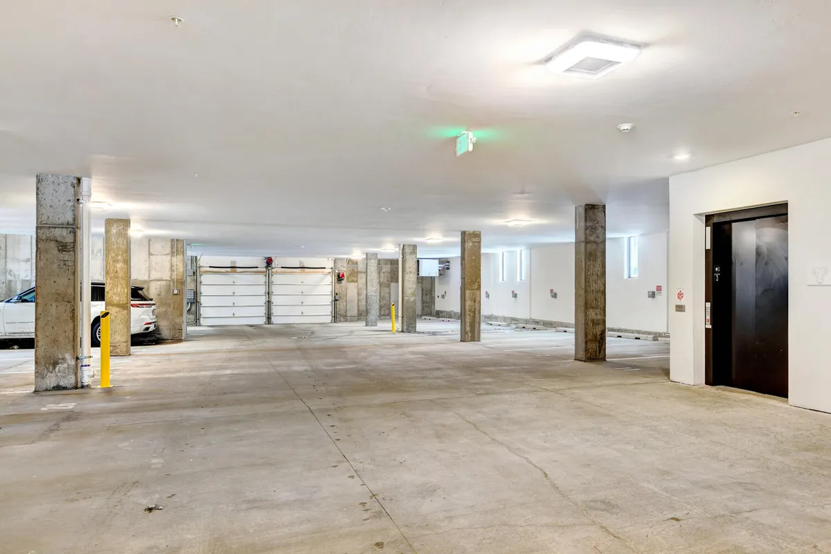 A spacious underground garage with marked parking spaces, a clearly visible garage door, support columns, and an adjacent elevator door. The well-lit, practical space emphasizes security and protection from the elements.