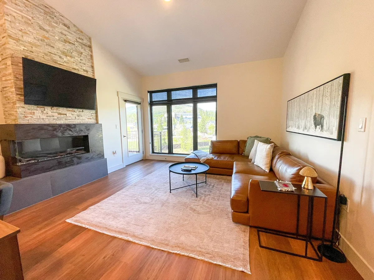 A modern living space with a large leather sectional sofa arranged around a stone fireplace. Expansive windows let in natural light and offer glimpses of the outdoors, making this area perfect for relaxing after a day of downtown adventures or enjoying après-ski camaraderie.