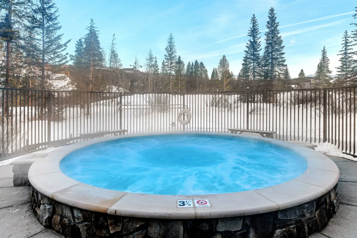 This image captures a serene outdoor hot tub surrounded by a snow-covered landscape and trees. The inviting steam rising from the tub contrasts beautifully with the winter scene, evoking relaxation and indulgence after a day of alpine activities.