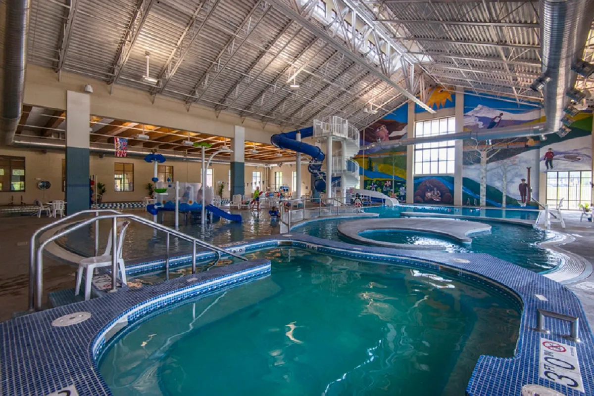 An energetic indoor pool scene at the Grand Park Rec Center, with children playing on a water slide, colorful murals, and a lively, family-friendly environment.