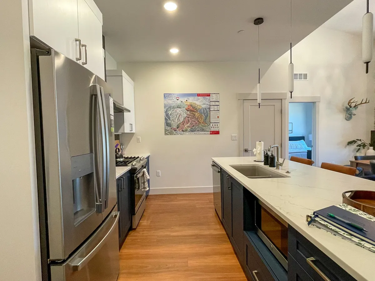 A contemporary kitchen with a stainless steel refrigerator, modern island, and a colorful wall map as a playful accent. The open layout welcomes group cooking sessions, entertaining, and shared meals, further encouraging communal experiences.